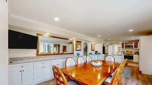 A spacious dining area with a large wooden table and chairs, a kitchen with white cabinets, and a large mirror above the table. - Pool, Beaches, OWA, Dining, and More | Palmaway (Foley)