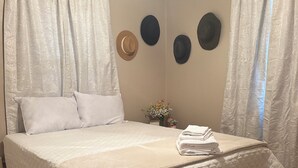 Un lit bien fait, recouvert d’une courtepointe blanche, une petite table de chevet ornée d’un vase de fleurs et un mur décoré de trois éléments circulaires.