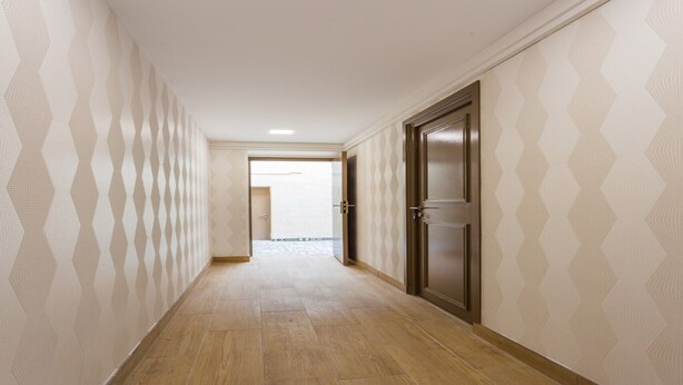 Un couloir avec un papier peint à motifs, un plancher en bois et une porte au fond.