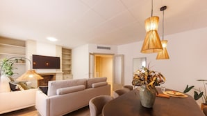 Ein modernes Wohnzimmer mit einer Couch, einem Esstisch mit Stühlen, einem an der Wand befestigten Fernseher und einem Kamin.