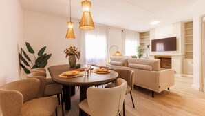 Ein modernes Wohnzimmer mit einem runden Esstisch, beigen Sofas und einem flachbildfernseher an der Wand.