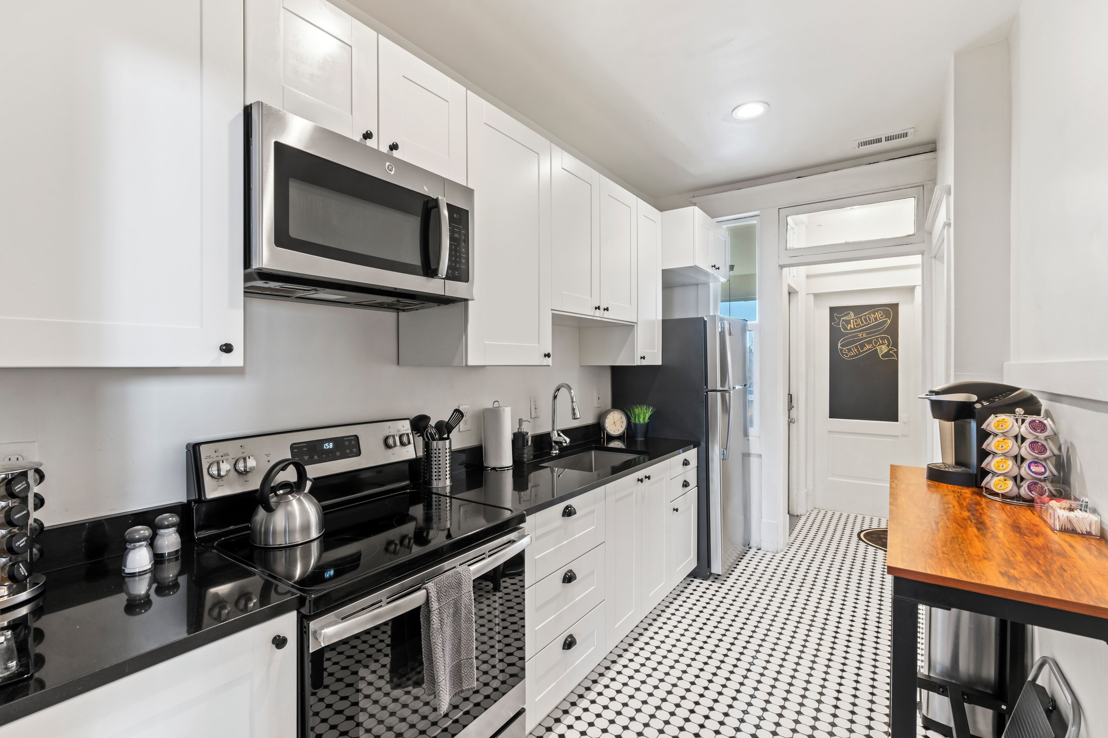 A modern kitchen with white cabinets, stainless steel appliances, a black countertop, and a patterned floor.