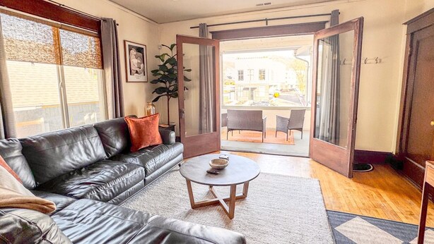 A living room with a leather sofa, a coffee table, and a view through an open door to an outdoor seating area.