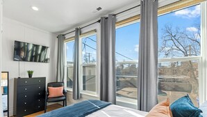 A bedroom with a bed, a dresser, a chair, and a TV on the wall.