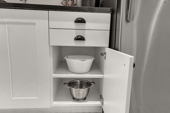 A kitchen with white cabinets, a stainless steel refrigerator, and a colander on the lower shelf.