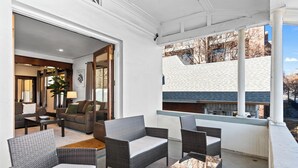 A covered outdoor seating area with wicker furniture and a view of a brick building.