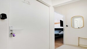 A hotel room with a white door, a keycard lock, a small table with a gold frame, and a mirror on the wall. - Cosy Cocoon for 2P with A/C - Near Montmartre (Paris)