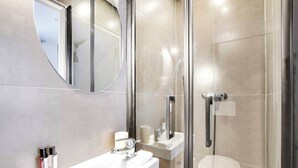 A modern bathroom with a glass-enclosed shower, a white sink with toiletries, and a large mirror.