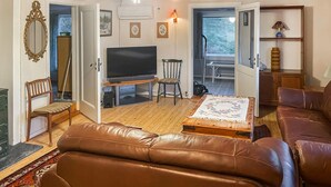 A living room with a brown leather sofa, a television, a wooden coffee table, and a chair. There is a door leading to a balcony with a view of trees. - 2 bedroom lovely home in Færvik (Færvik)