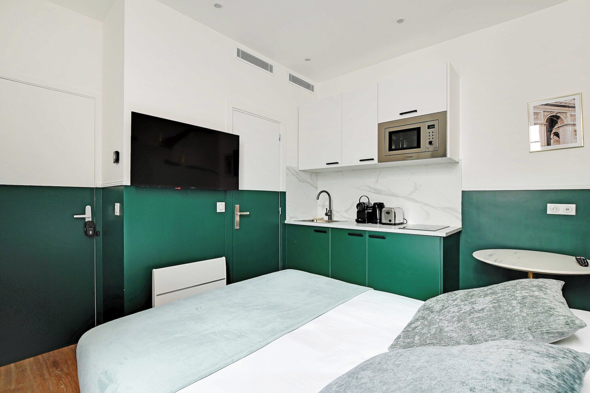 A modern hotel room with a bed, a small desk with a microwave, and a sink.