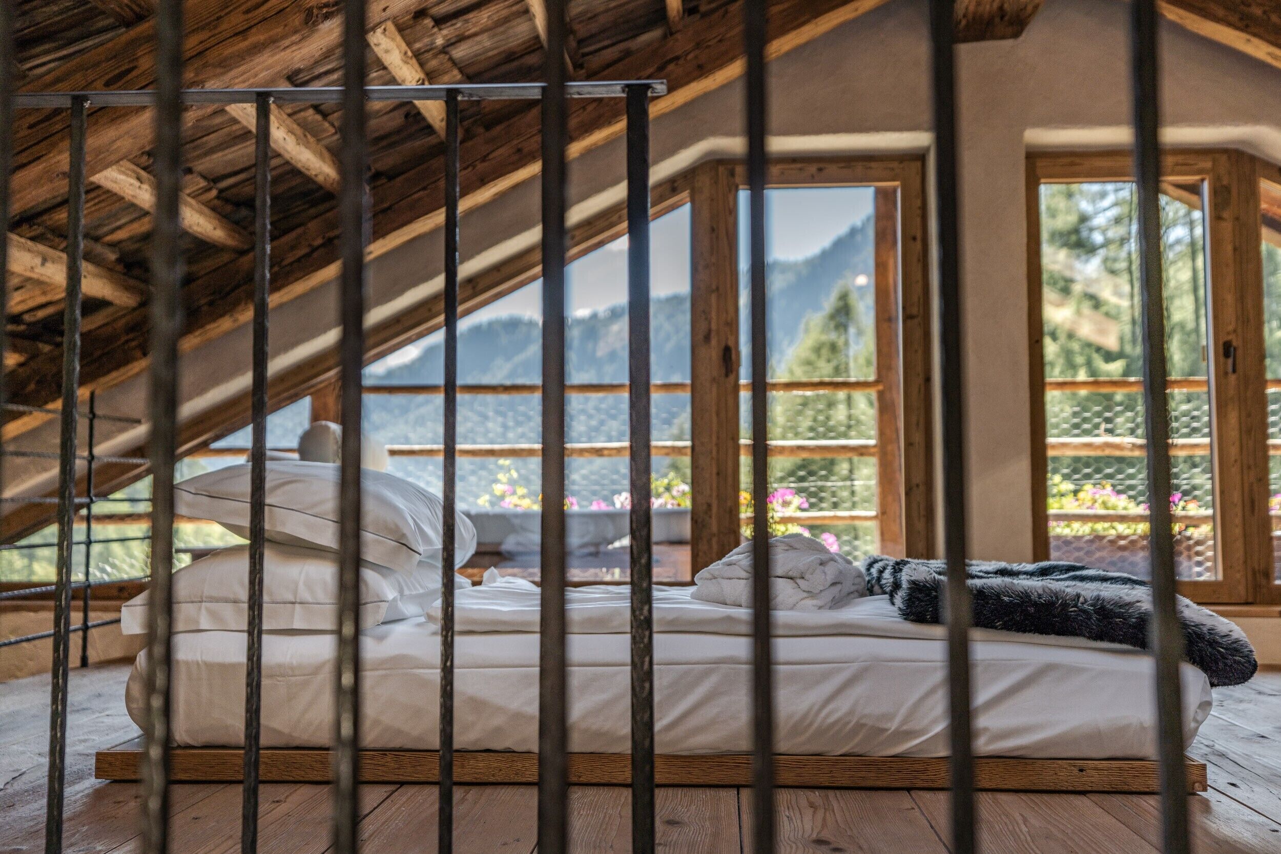 Een bed in een kamer met een schuine balklaag en grote ramen.