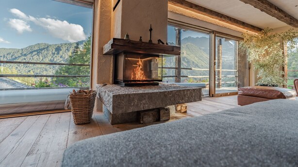 A stone fireplace with a fire, large windows with mountain views, and a cozy seating area.