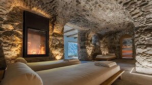 A stone-walled room with a bed, a fireplace, and a view of the outdoors.