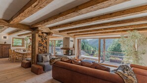 A spacious living area with a wooden ceiling, large windows, a sofa, and a dining table.