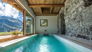 A spa pool with a wooden ceiling, stone walls, and a view of mountains.