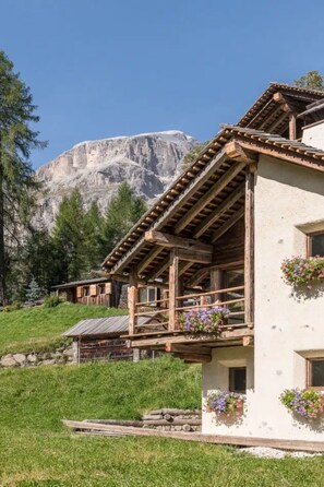 Un rustico chalet con un balcone in legno, immerso nel verde e affacciato sulle montagne.