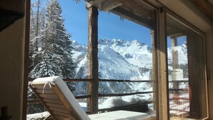 A wooden-framed window with a view of snow-covered mountains and trees.