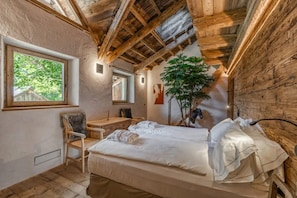 A rustic room with a wooden ceiling, a bed, a desk, and a chair.