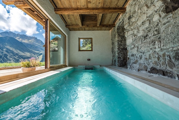 A spa pool with a wooden ceiling, stone walls, and a view of mountains.