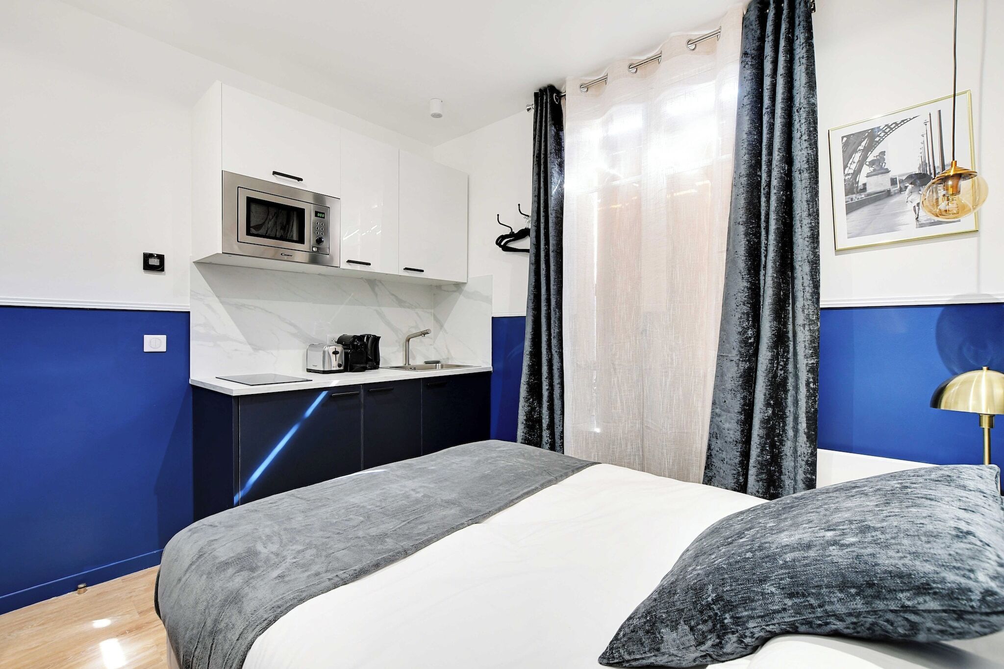 A modern hotel room with a bed, a small kitchenette, and a bathroom.