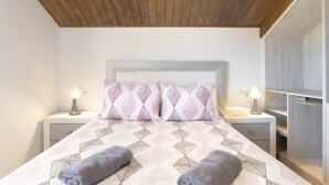 A bedroom with a wooden ceiling, a bed with patterned bedding, two bedside lamps, and a nightstand with a basket. - Holiday Home 'Ro' with Private Pool, Wi-Fi and Air Conditioning (Conil de la Frontera)