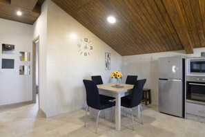 Eine Küche mit Esstisch, Stühlen, einer Uhr, einem Kühlschrank und einer Holzbalkendecke.