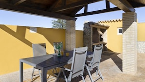 An outdoor patio with a table and chairs, a brick oven, and a yellow wall. - Holiday Home 'Ro' with Private Pool, Wi-Fi and Air Conditioning (Conil de la Frontera)