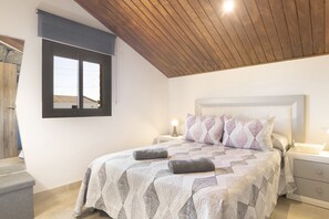 Ein Schlafzimmer mit Bett, Nachttischen, einem Fenster und einer Holzbalkendecke.
