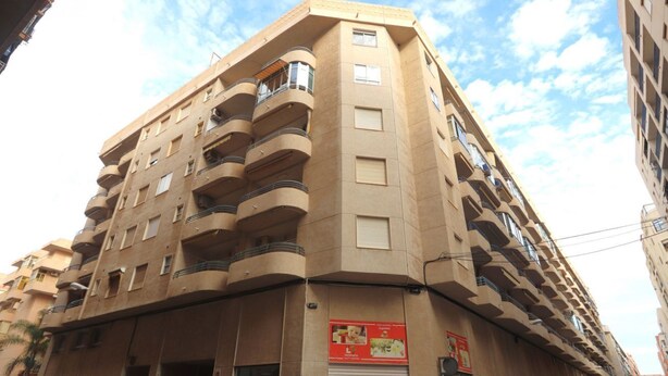 Un edificio de varios pisos con balcones, una tienda cerrada en la planta baja y un cielo despejado.