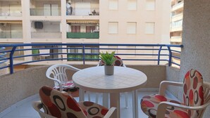 Un balcón con una mesa redonda y sillas, una planta en maceta, y vista a un edificio con varios balcones.