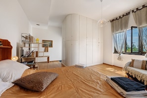 Un dormitorio con cama, escritorio, armario y ventana con cortinas.