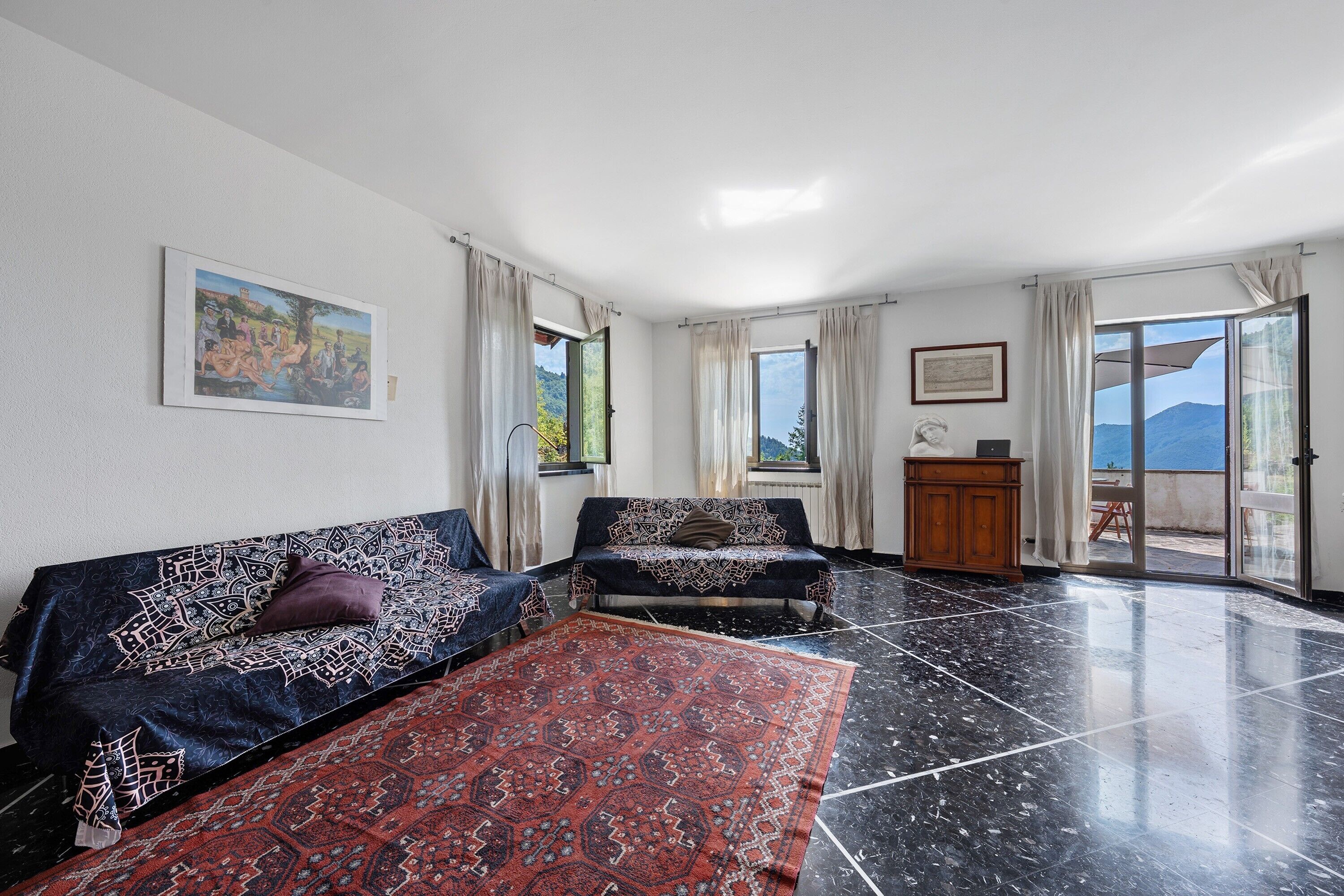 A room with a sofa, a patterned rug, a cabinet, and a view through a glass door.