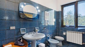 Ein Badezimmer mit Waschbecken, Spiegel, Toilette, Bidet und einem Fenster mit Blick auf Bäume.