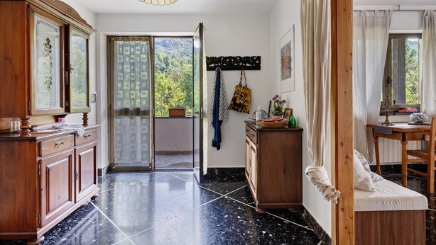 Una stanza con un armadio in legno, una porta vetrata che dà su un balcone, un letto a baldacchino e un tavolo con una lampada.