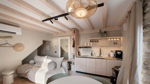 A bedroom with a bed, bedside table, and a small table with a chair. There is a kitchen area with a counter, cabinets, and a hanging light fixture. - Apartment Oliva (45 m2) with shared terrace, sauna and lake view (Brenzone sul Garda)