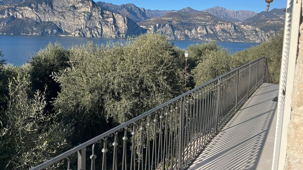 A coastal view with a metal railing, a lamp post, and a mountainous backdrop. - Apartment Oliva (45 m2) with shared terrace, sauna and lake view (Brenzone sul Garda)