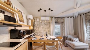 A modern kitchen with a dining table, chairs, and a built-in oven. There is a stone wall and a window with curtains.