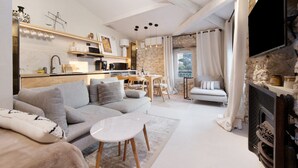 A modern living room with a sofa, coffee table, fireplace, kitchen area, and dining table.