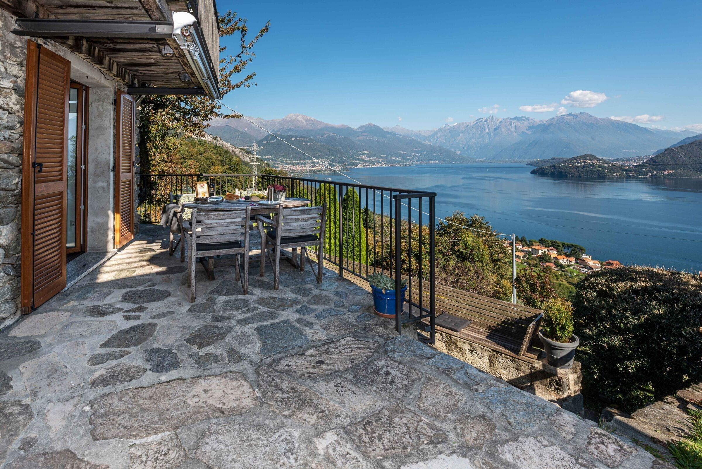 Une terrasse en pierre avec une table et des chaises, d’où l’on a vue sur un lac et, au loin, sur des montagnes.