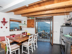 Un coin repas avec une table et des chaises en bois, une cuisine équipée d’une cuisinière, et une vue sur les montagnes par une porte vitrée.