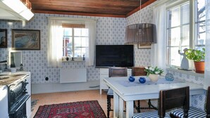 Une cuisine chaleureuse avec un plafond en bois, un papier peint à motifs, un grand téléviseur à écran plat, une table à manger avec des chaises et un tapis rouge à motifs.