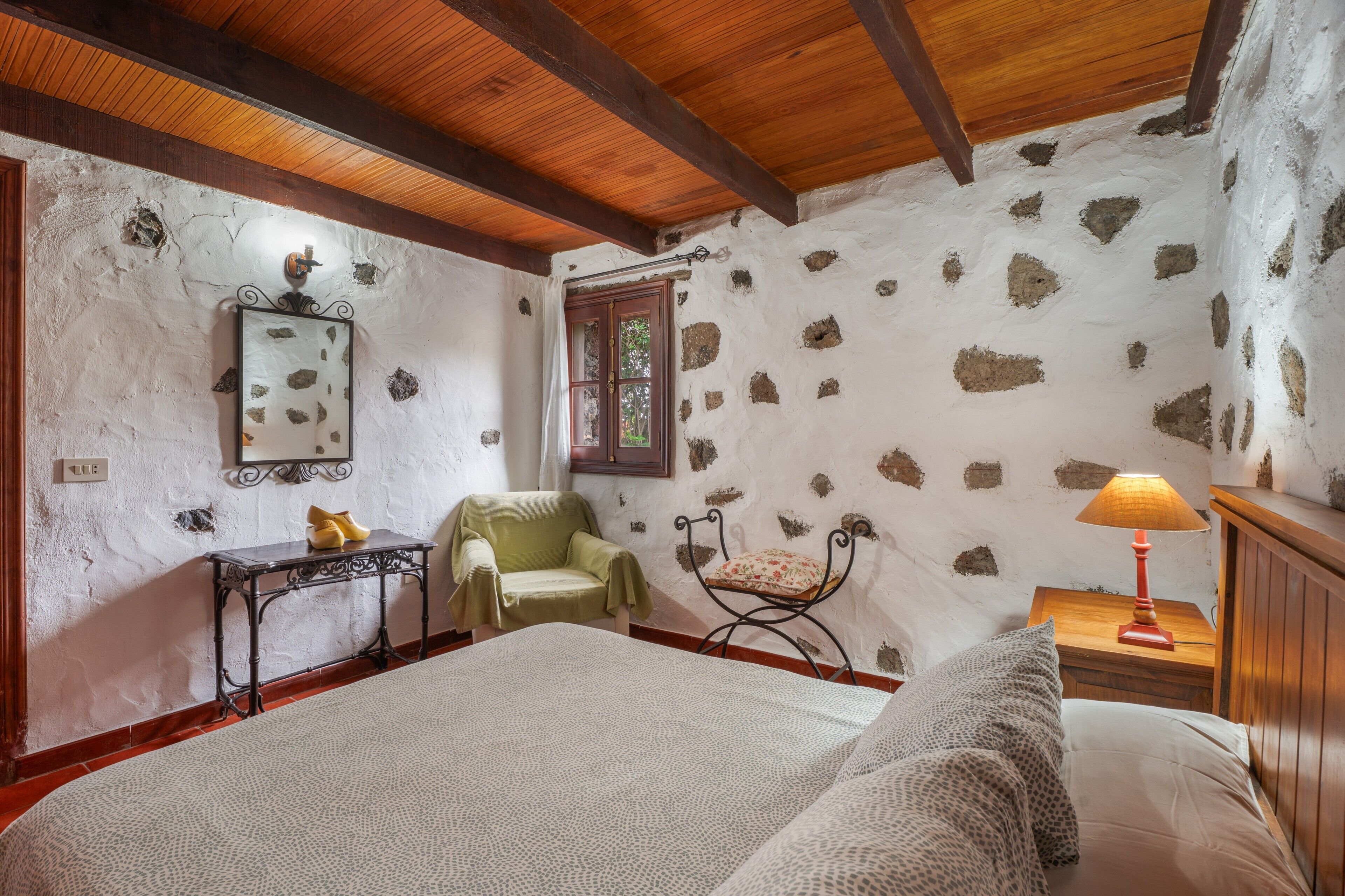 Una habitación con cama, una silla, una mesa, una lámpara y una ventana.