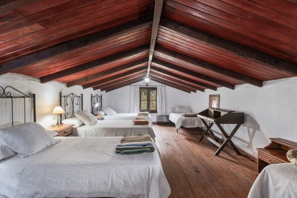 Habitación con vigas de madera, dos camas, un escritorio y una ventana.