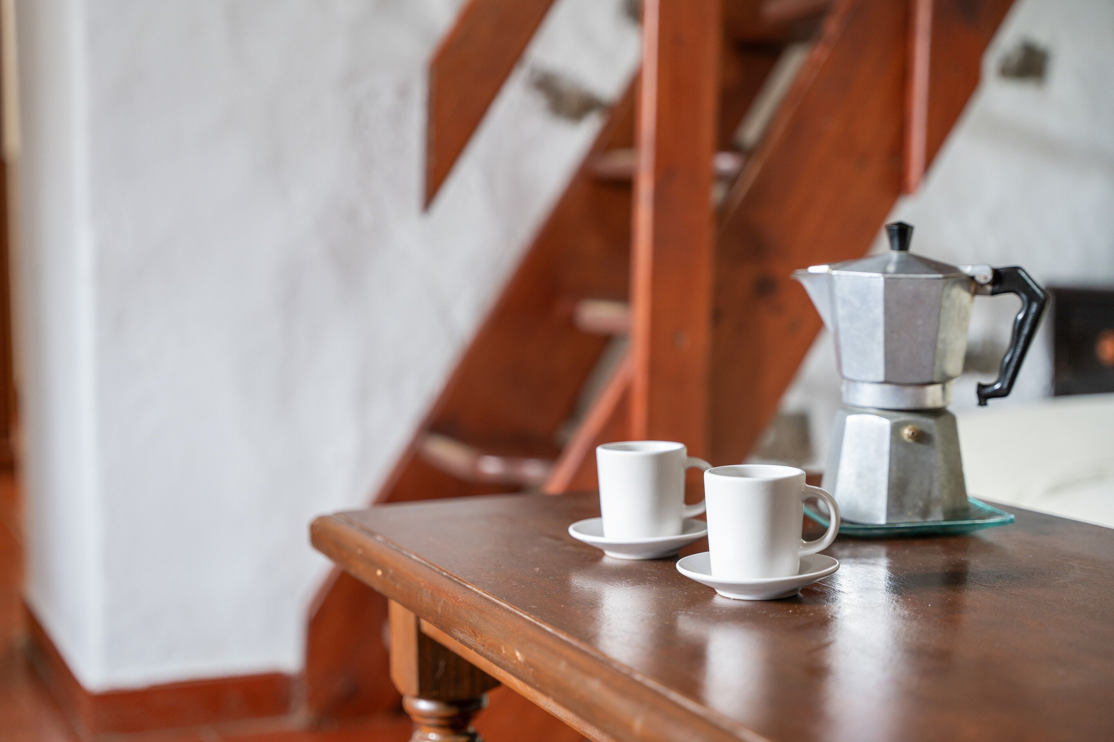Uma mesa de madeira com uma cafeteira e duas chávenas brancas num pires.