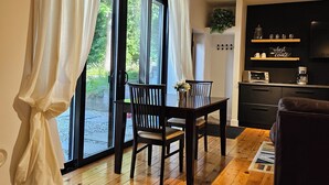 Un coin repas avec une table et des chaises en bois, une cuisine avec des meubles sombres et une vue à travers de grandes portes vitrées.