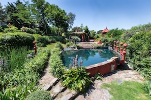 Um jardim com piscina, caminho de pedra e lanternas vermelhas.