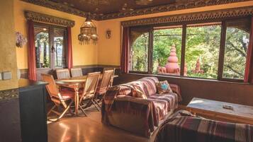 A room with a dining table, chairs, a sofa, and a window with a view of greenery and a pink pagoda.