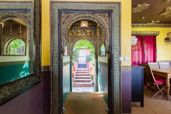 Uma porta ornamentada com desenhos intrincados, uma escadaria que leva a um quarto e uma sala de jantar com mesa e cadeiras.