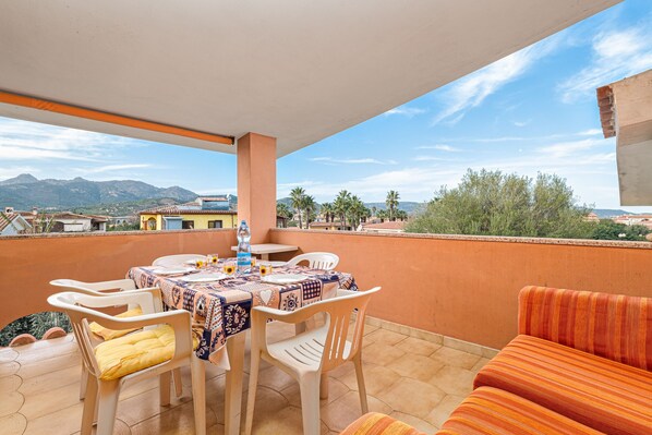 Une terrasse avec une table et des chaises, un canapé et une vue sur les montagnes et les bâtiments.