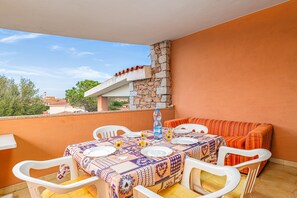 Un balcon avec une table dressée pour quatre personnes, des chaises blanches et un canapé rayé orange.